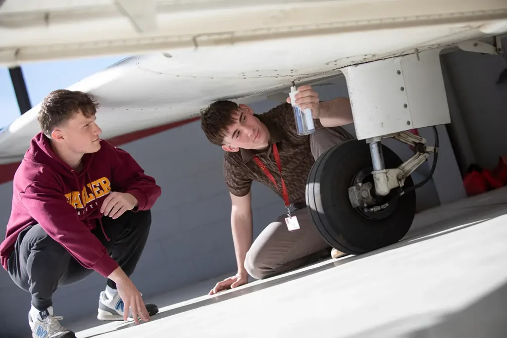 Student and instructor working on the underside of the plane near the wheel